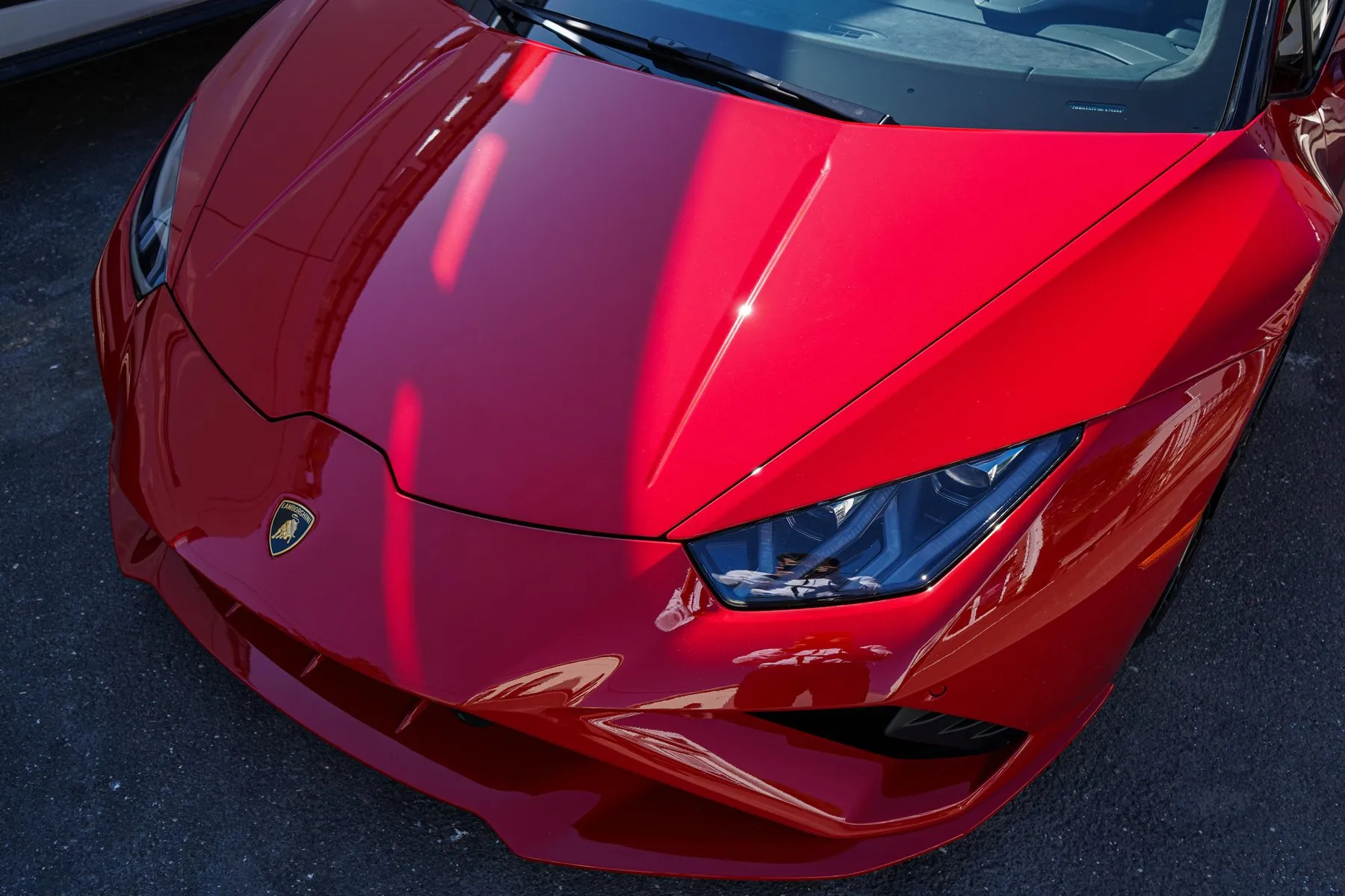 Close crop of the hood and headlight of a red Lamborghini Huracán, reflecting the sky.